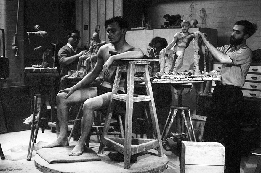 A black and white photo of a group of students sketching a life model.