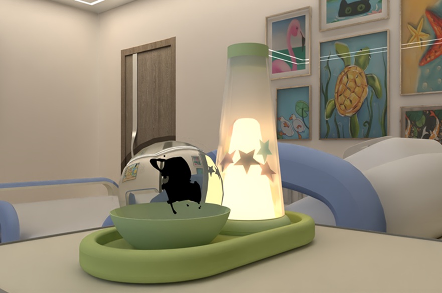 A hospital room with brightly coloured pictures on the wall. On a hospital table over a bed there are two objects - one a lamp containing stars, the other a bowl with a clear round object it in.