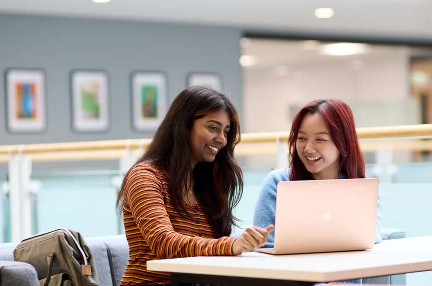 Two students working and smiling together in an open study space.