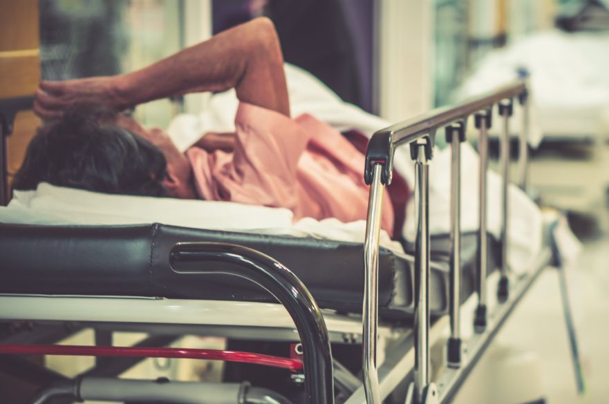 Patient lying on a hospital bed in a corridor, busy hospital, NHS pressures