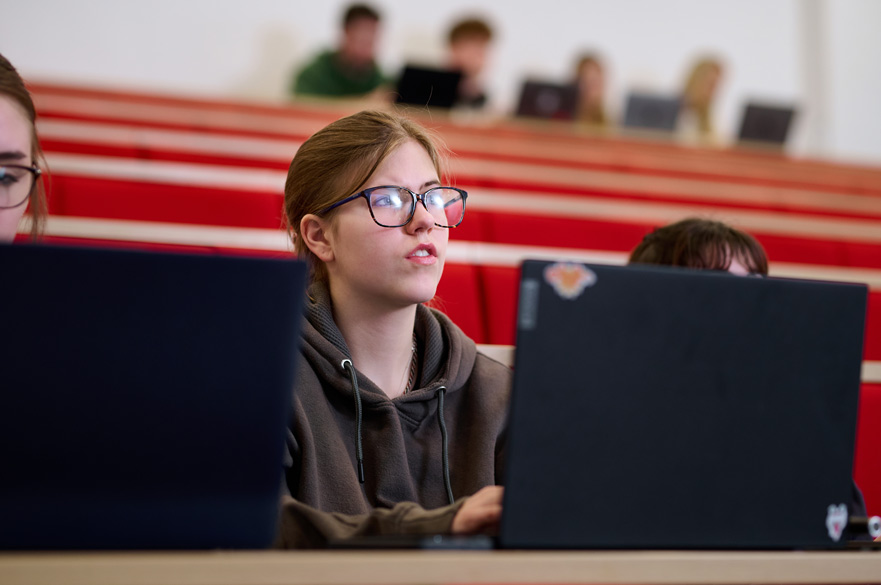 A student sitting with a laptop in front of them in a lecture theatre.
