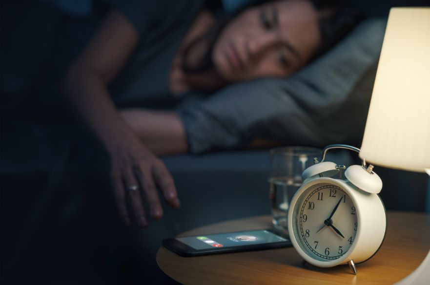 Woman lying in bed awake and in the dark, her phone is ringing and it says five past four on the bedside clock