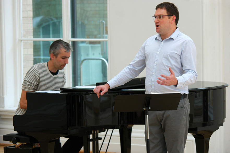 A male stood in front of a piano singing.