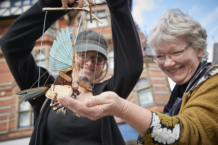 A lady holding a marionette bird in her hand.