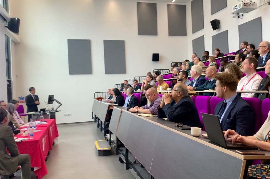 Lecture theatre with visitors seated and watching panel of speakers