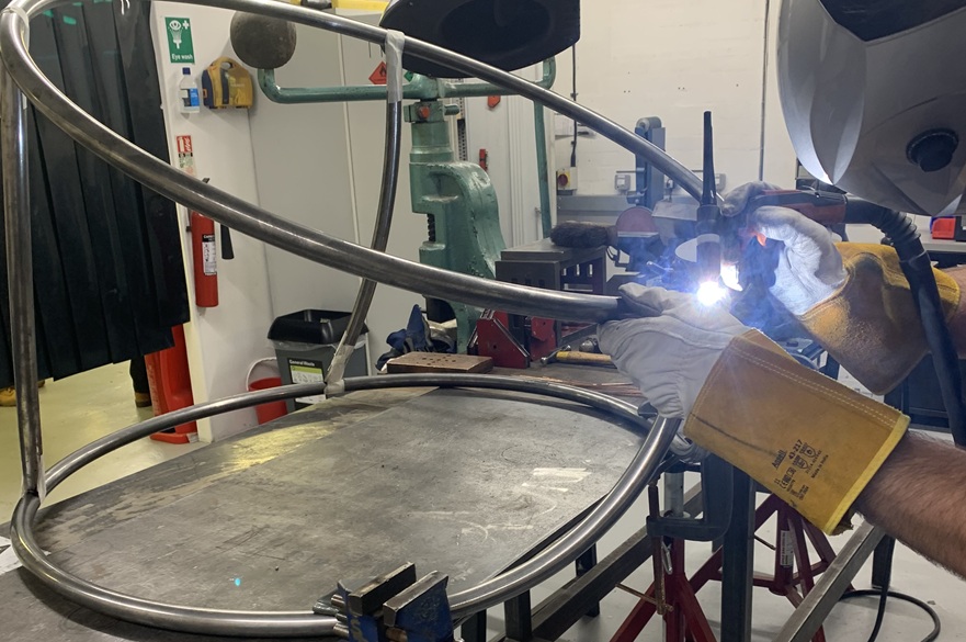 The circular metal frame of a gaming chair being worked on in a workshop.