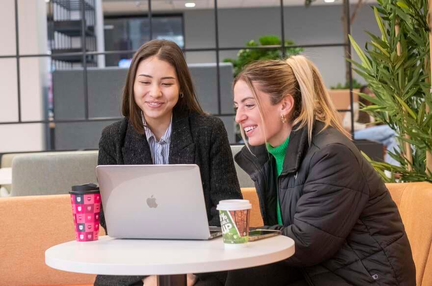 Two students smiling while looking at a laptop screen.
