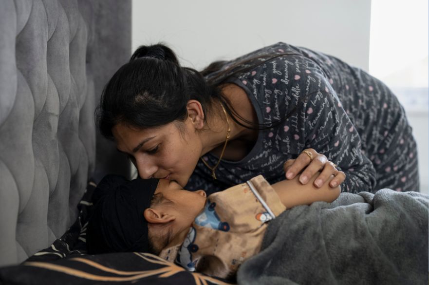 Mother kissing her son goodnight while he lies in bed with his eyes closed