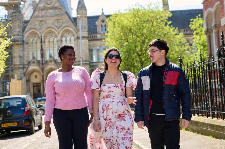 Three students walking and smiling with Arkwright building behind them