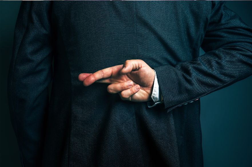 Back of a man in a suit with his fingers crossed behind his back