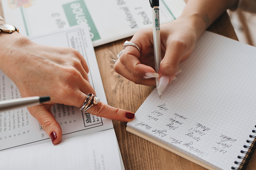 A lady writing in her notepad who has been guided by another lady. 