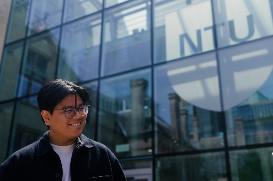 Student walking outside Newton Building with NTU shield behind him