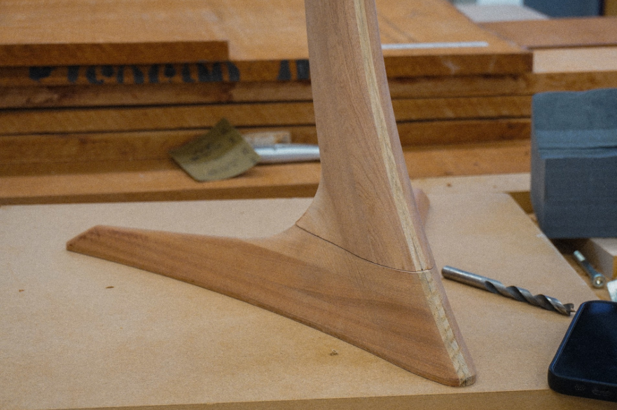 The wooden base and part of the stand of a drum practice pad made out of wood.