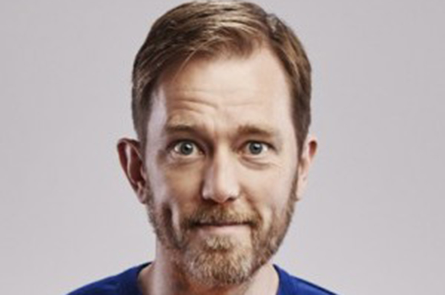 Alun Cochrane facing the camera in front of a white background. 