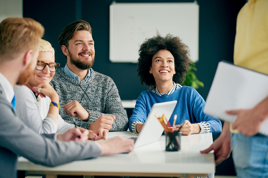Group of people in an office sitting around a desk and smiling