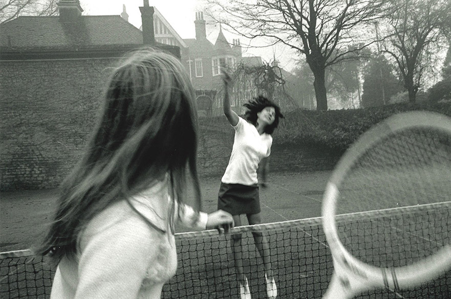 A black and white photograph of two women playing tennis on an outdoor court.