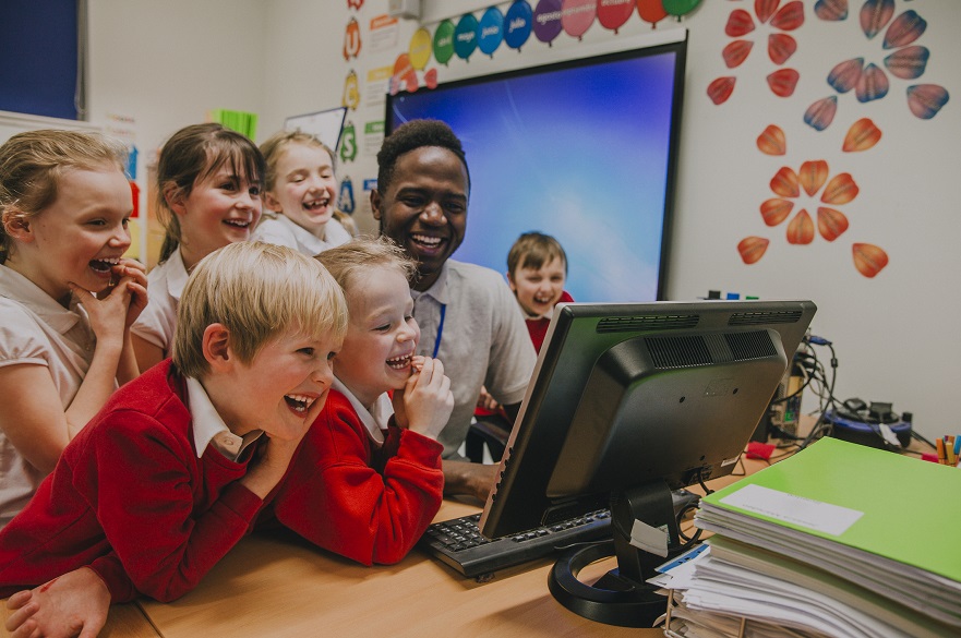 Male teacher with primary students around a computer