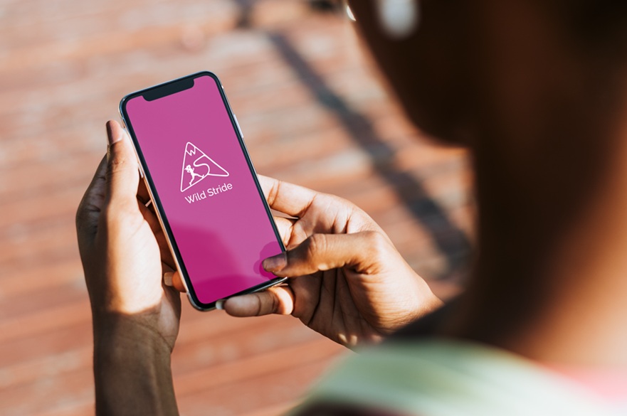 A person in running wear is holding a mobile phone displaying an app for trail runners.