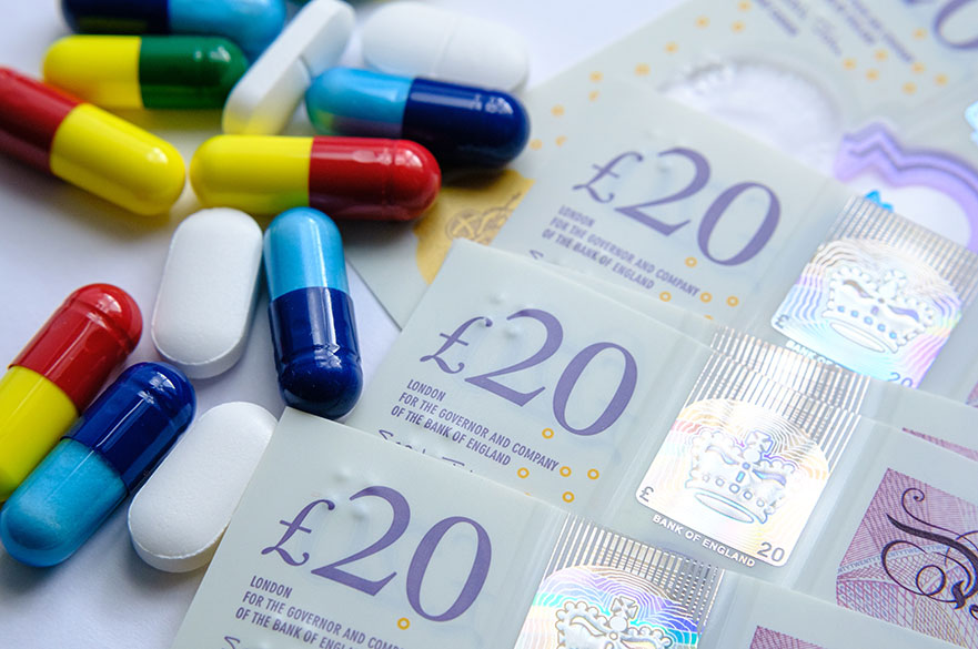 Pile of different colouful pills placed next to 20 british pound banknotes. Illustrative for cost of medical bills, health insurance