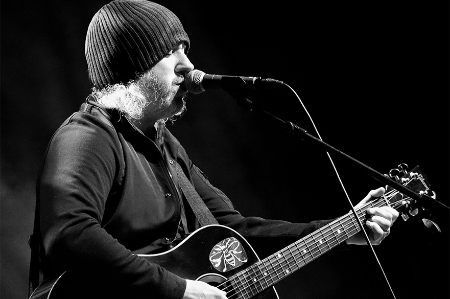 A black and white image of a man playing the guitar and singing.