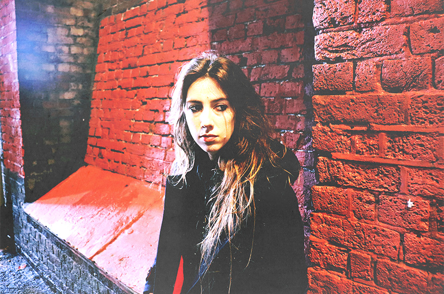 A woman leaning against a red brick wall.