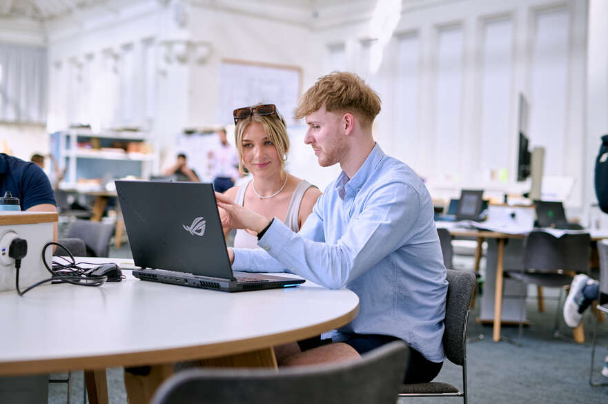 Two students looking at and discussing what's on laptop screen