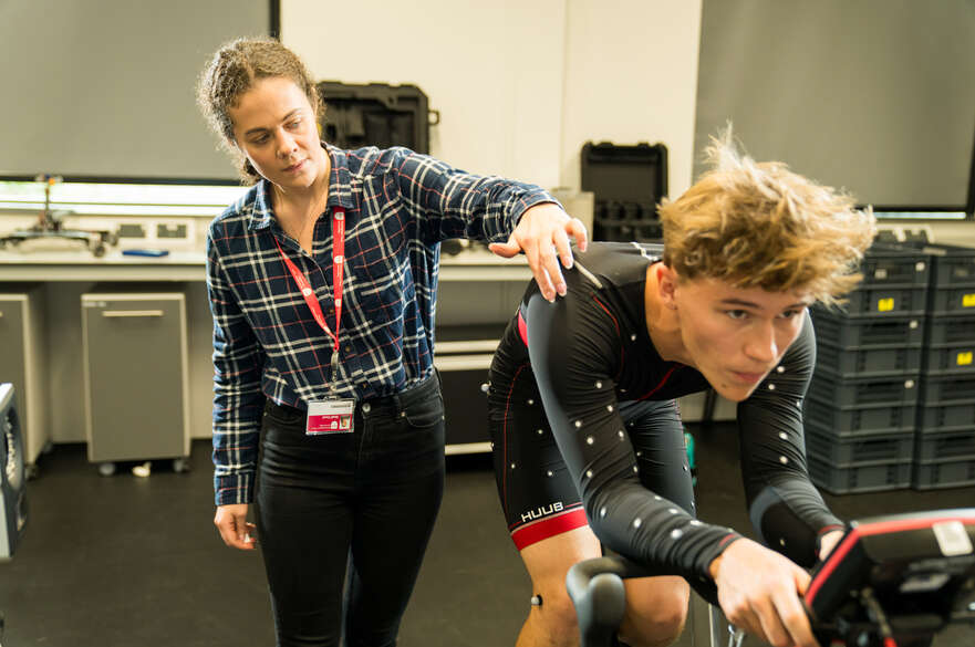 A sport science student on an exercise bike with academic observing.