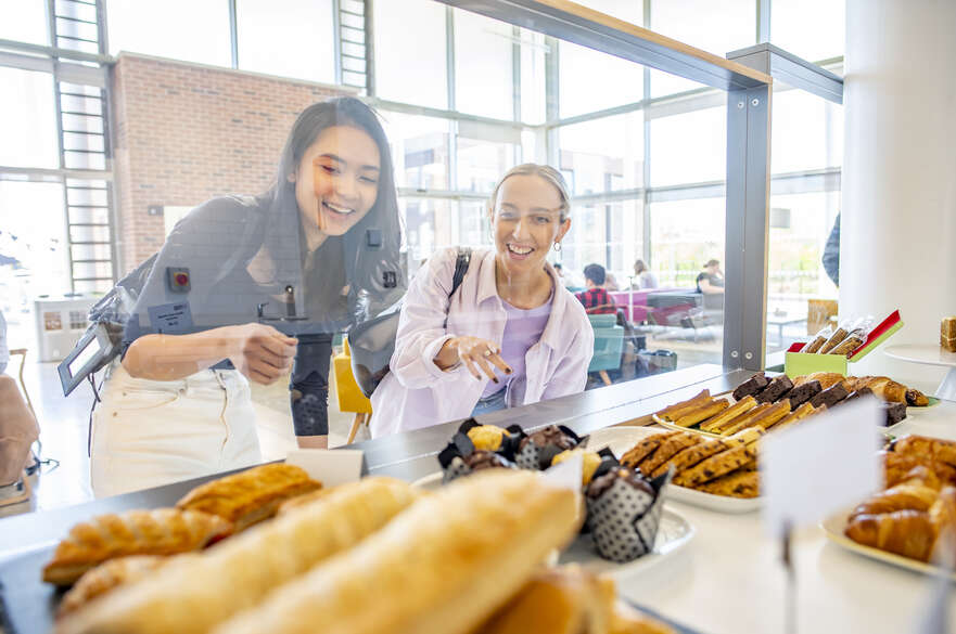 Two students look through a glass cabinet at the food available