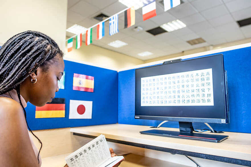 A student learning a new language, using a book and a computer.