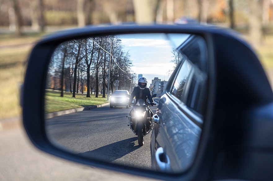 Mutual passing, motorcycle and vehicle with dazzle lighting overtaking the car, view in a side mirror