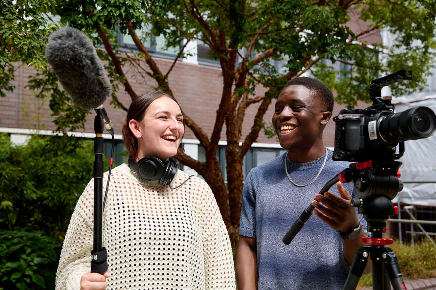 Two students laughing whilst holding filming equipment
