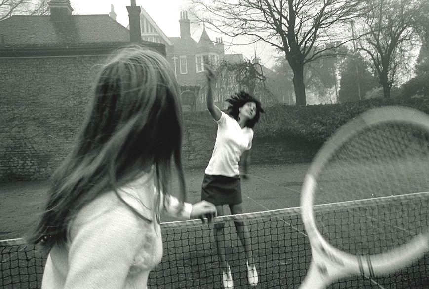 A black and white image of two women playing tennis outdoors