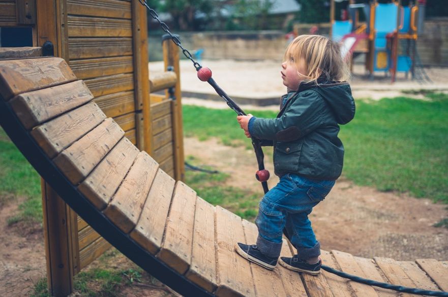 Small boy pulling himself up a rope on play equipment
