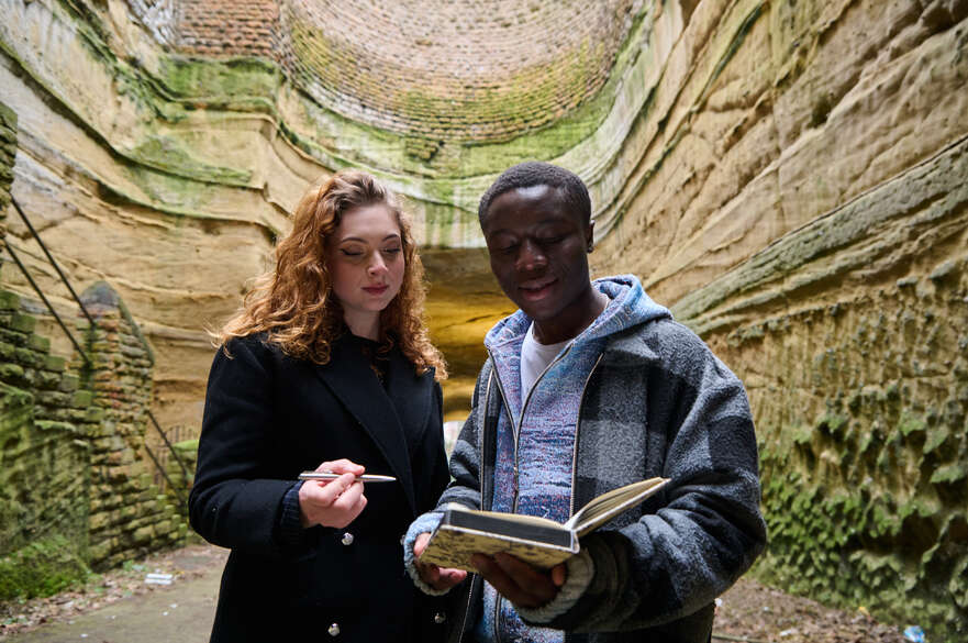 Two students reading a book inside of a historic cave