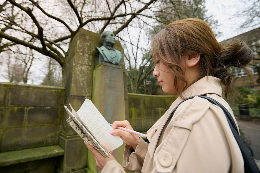 Creative Writing student writing in her notebook standing next to a statue
