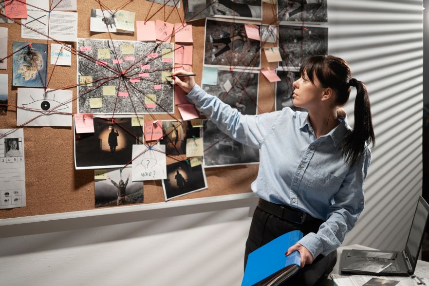 Image showing a law enforcement officer infront of a board with photos and string connectors indicating a criminal investigation