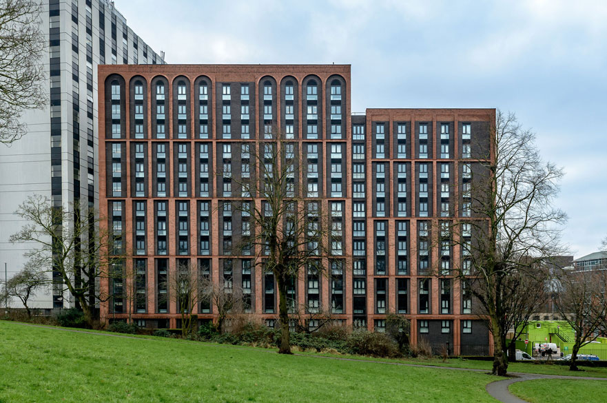 A multi-storey, red brick building beside a grassy park area.