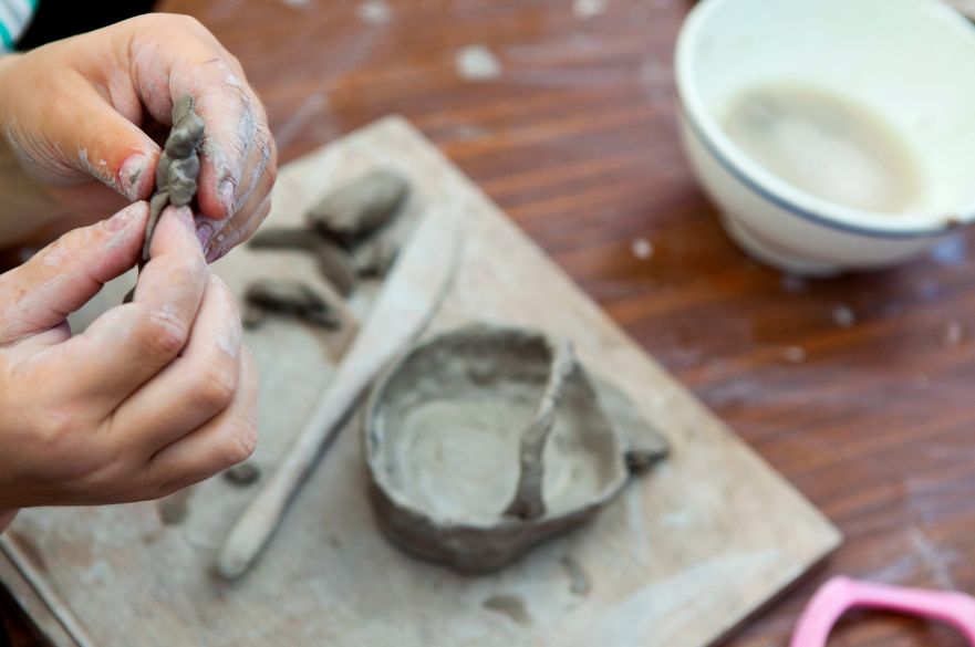 Two hands molding a piece of clay with pottery and water in the background.
