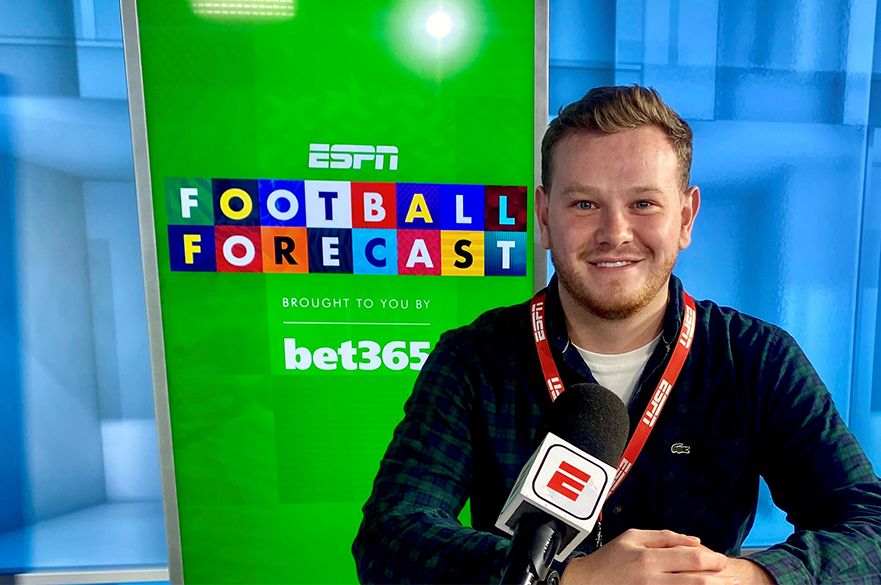 A photo of a smiling male NTU alumni who is standing in an ESPN TV studio. The screen behind him reads: