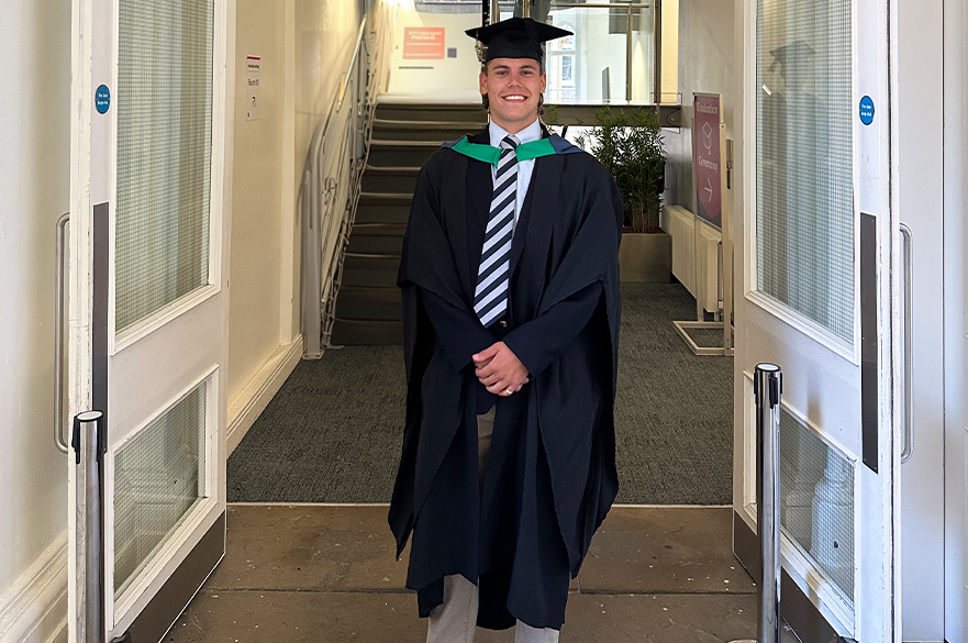 Sam posing in his graduation gown underneath the ADBE sign