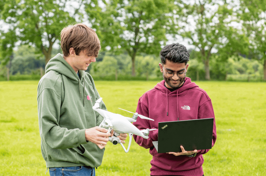 Two students holding a drone and laptop