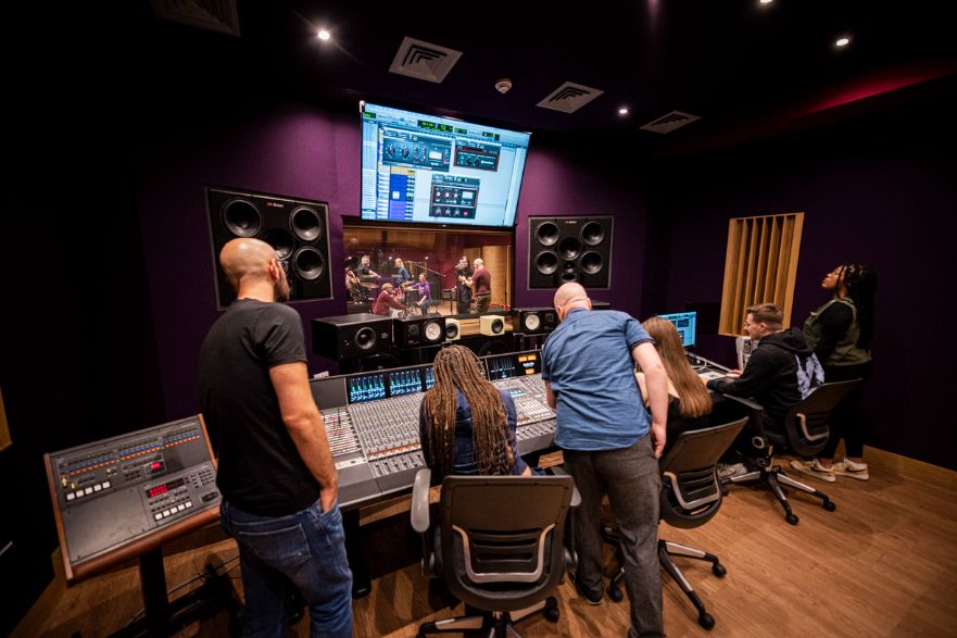 Students working in a recording studio while a band plays in a recording booth