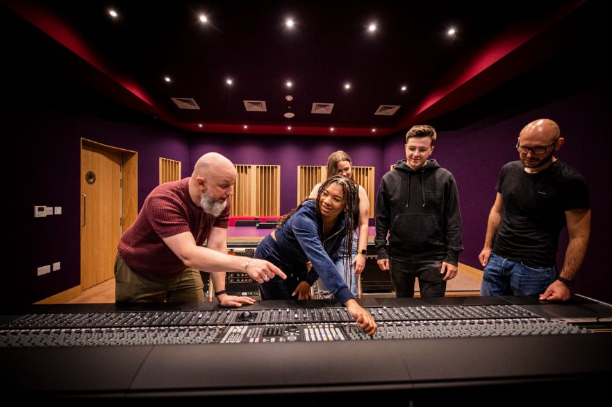 Lecturer assists a student with a mixing desk while other students watch