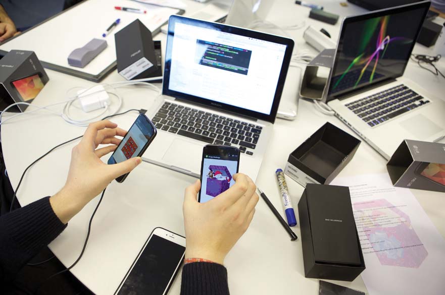 Person holding 2 smartphones in front of laptop