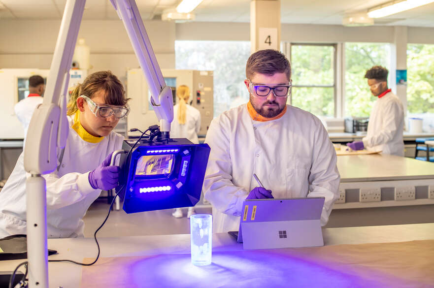 Two forensic science student using specialist equipment to identify prints on a glass