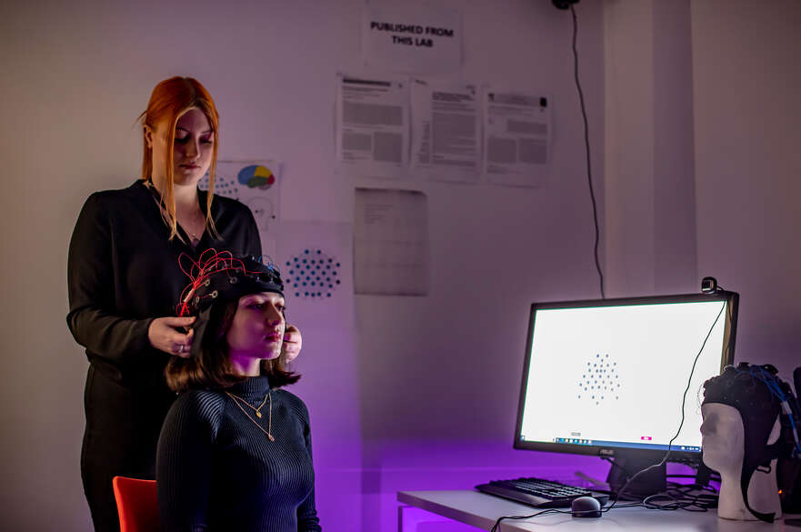 Student in a Psychology lab wearing a headset, supported by a member of staff