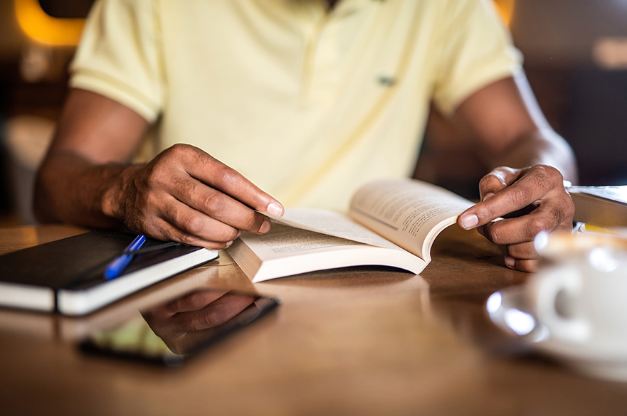 Someone sat reading a book at a table.