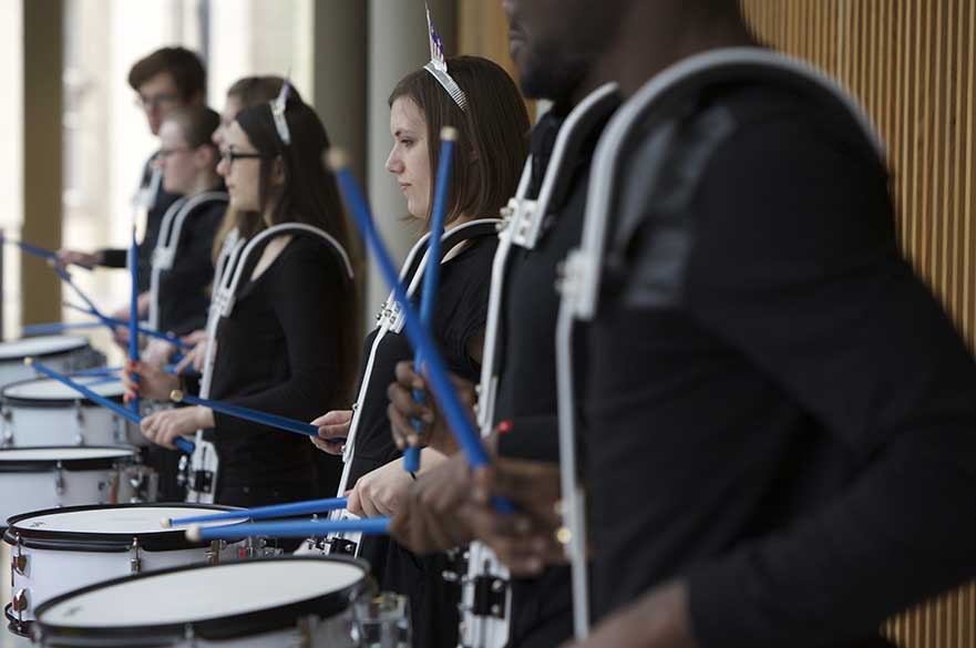 Male and female students playing snare drums in a line.