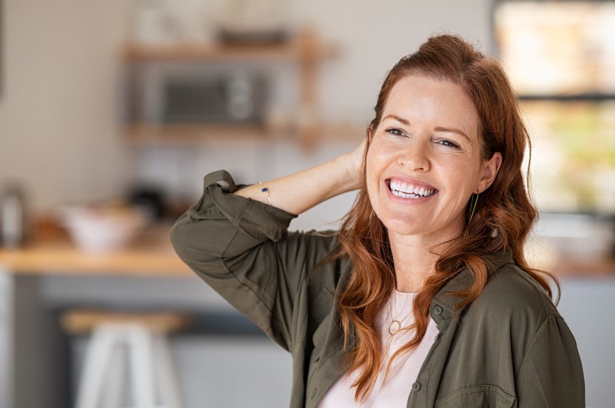 A smiling lady standing in a kitchen with her hand on her head