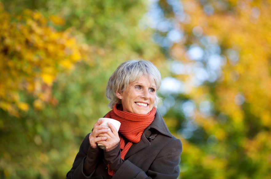 A smiling lady holding a cup standing in front of a tree